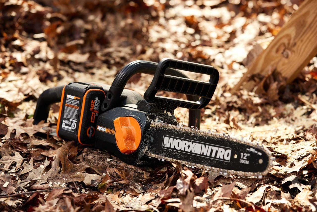 A Worx Nitro 12-inch chainsaw resting on fallen autumn leaves, showing its orange and black design.