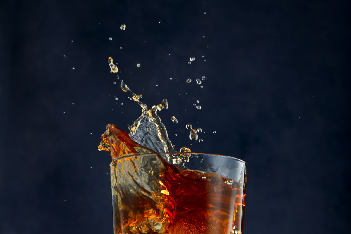 Commercial food photograph of whiskey splashing out of rocks glass shot in studio on blue background