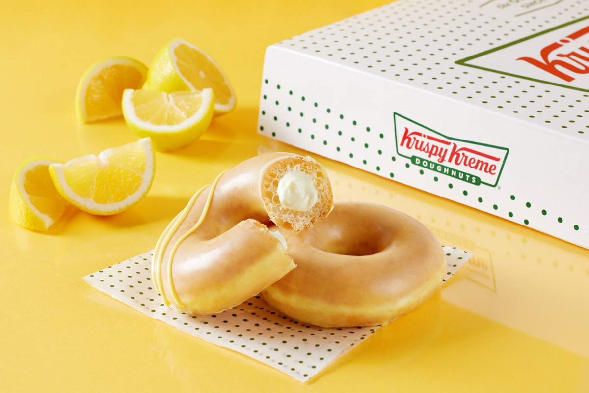 Professional commercial photography of lemon glazed Krispy Kreme doughnuts against yellow reflective backdrop with lemons