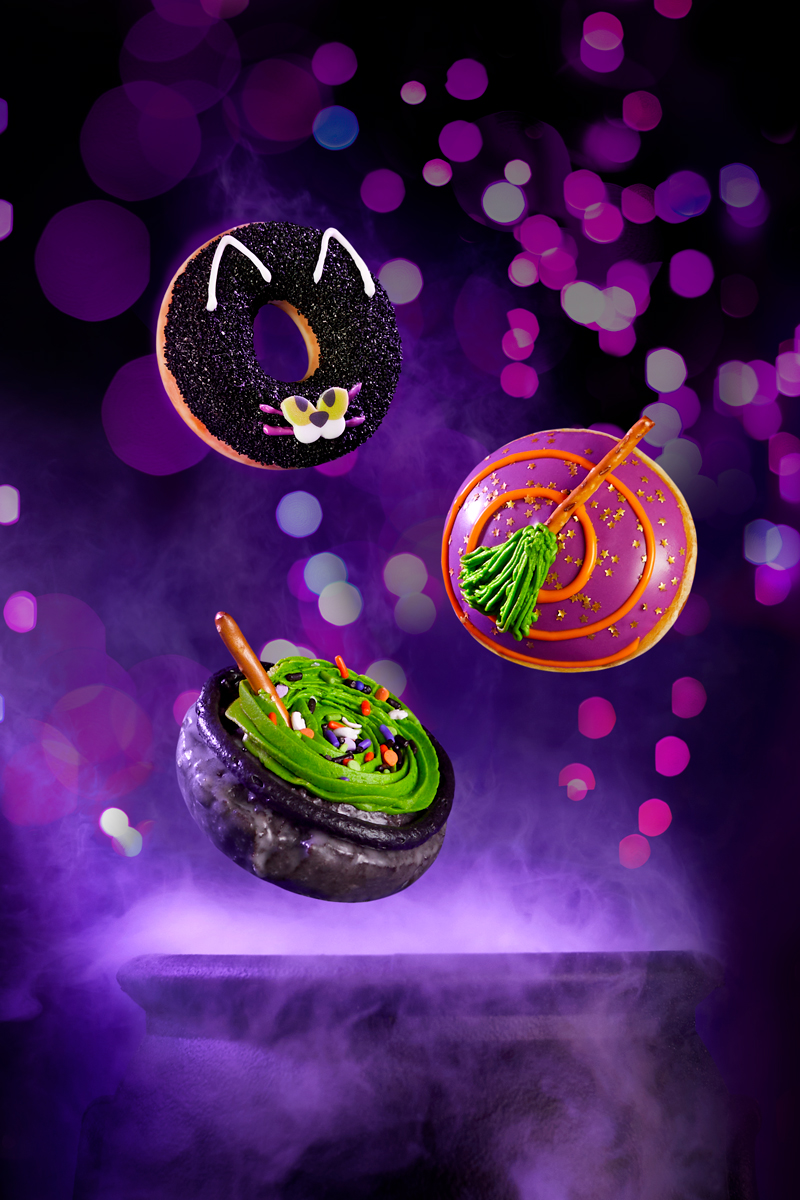 Commercial food and product photography of floating Krispy Kreme Halloween doughnuts above witches cauldron with purple background and smoke for advertising and signage purposes