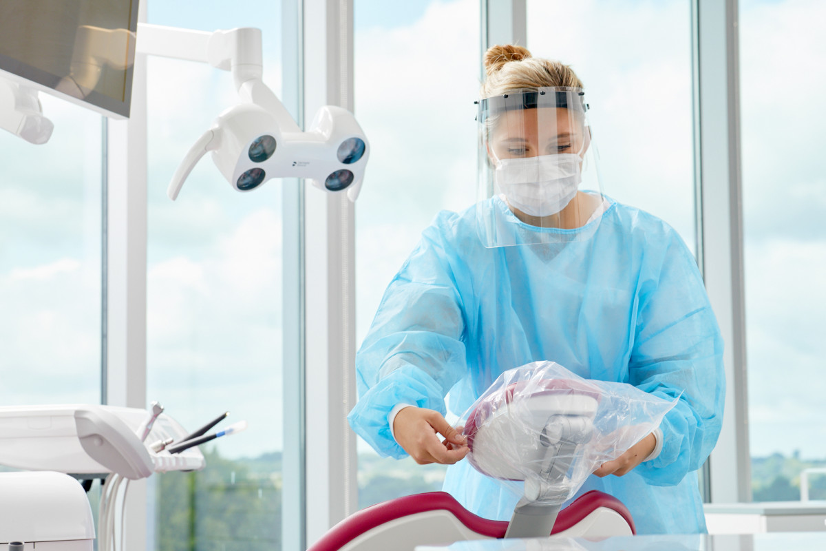 Commercial lifestyle photography of dental assistant in complete PPE preparing a dental exam chair