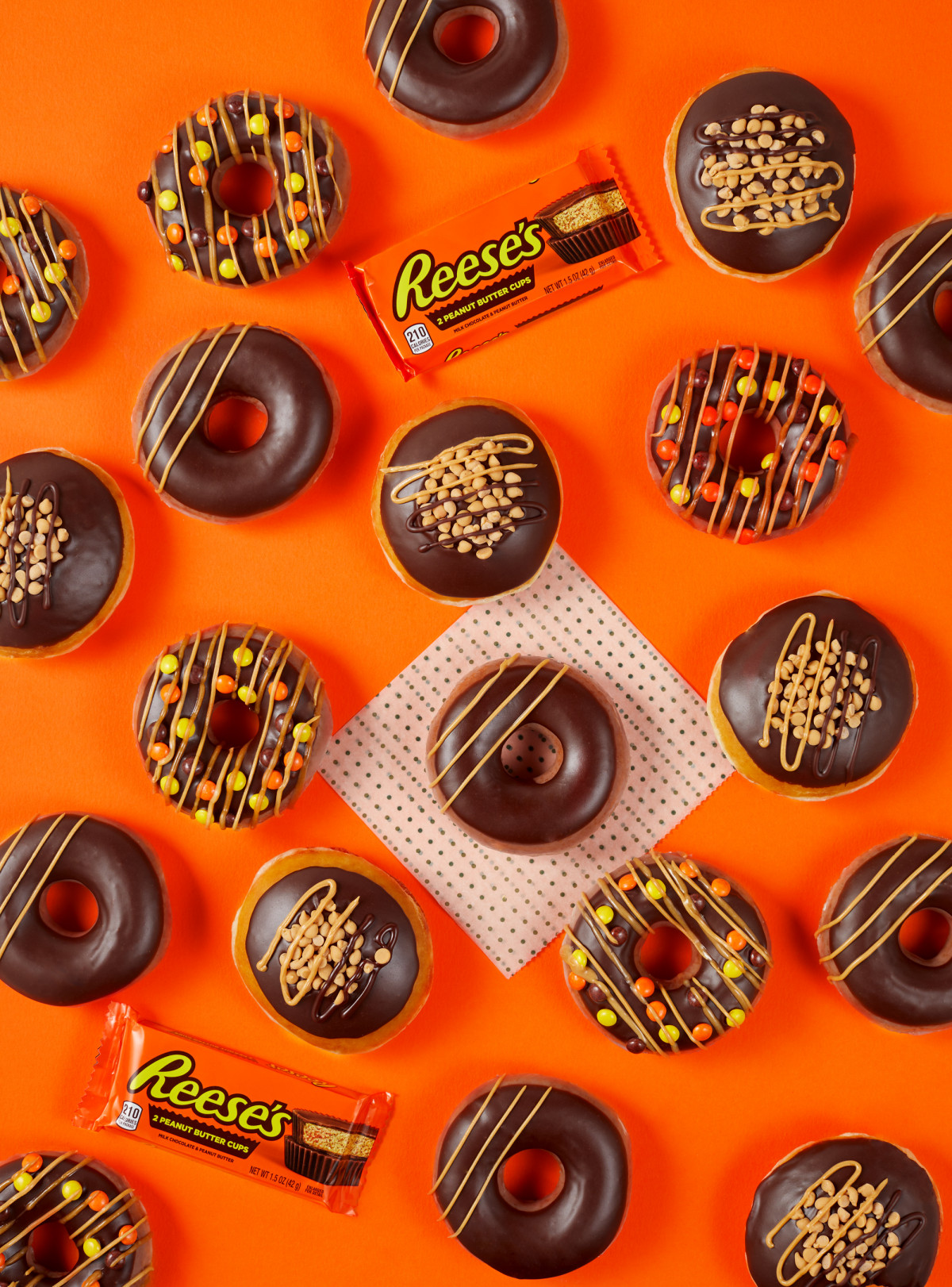 Commercial food photography of Krispy Kreme Reese's flavored doughnuts against an orange background