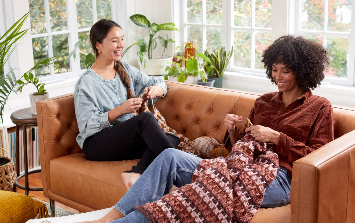 Editorial Lifestyle Photography of two women knitting on leather couch in sunroom smiling and laughing.