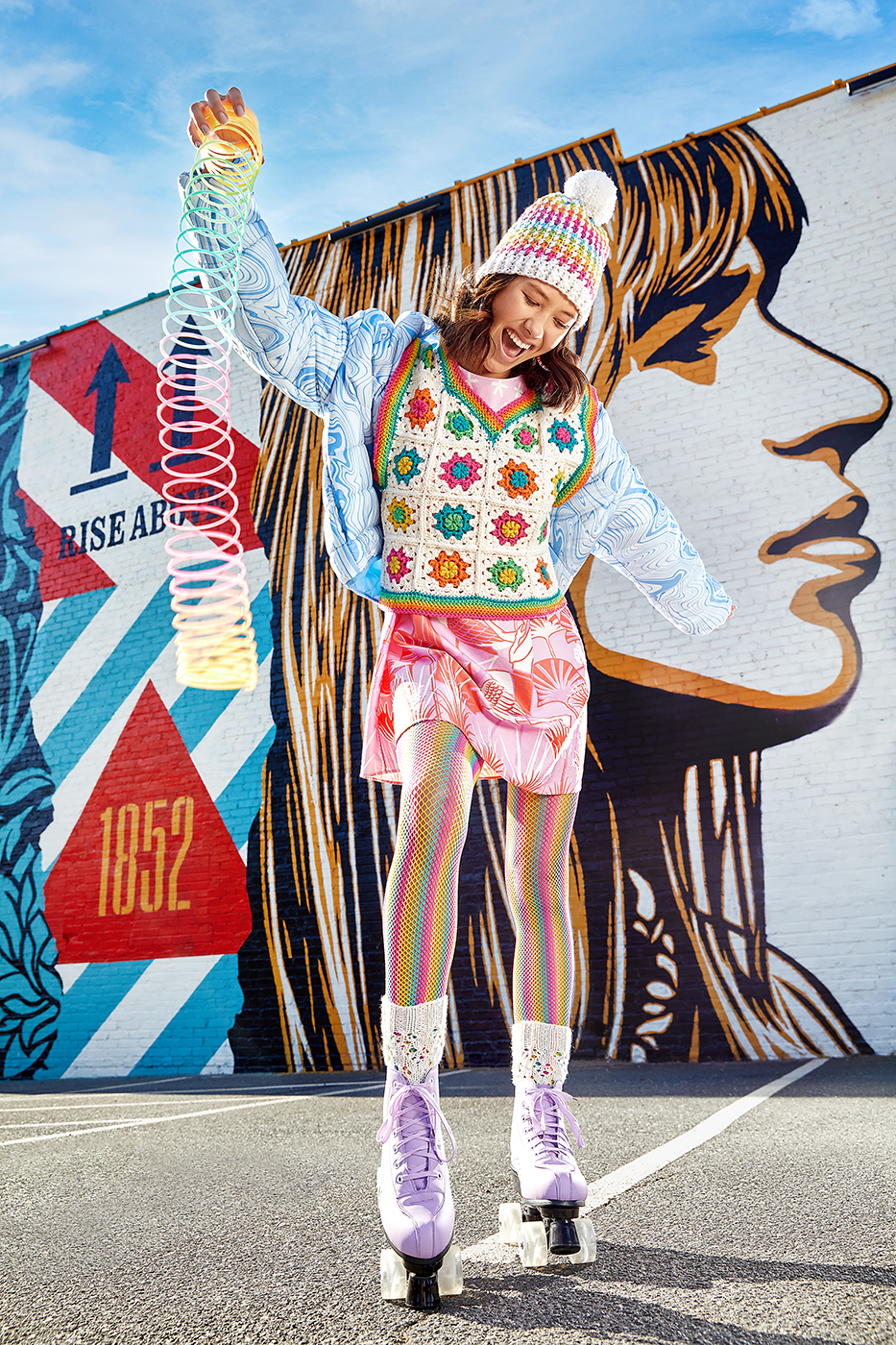 commercial fashion and apparel photography of girl in roller skates with slinky in front of Shepard Fairey mural