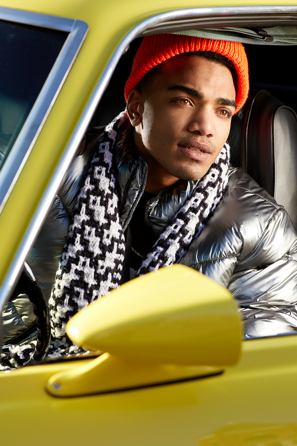 commercial lifestyle photography of man in yellow car with black and white scarf and orange knitted hatman in yellow car