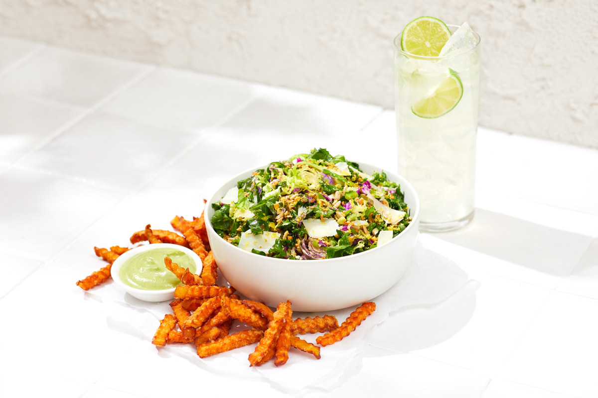 commercial food photography of bowl of salad and sweet potato fries with lemonade on white tile background.