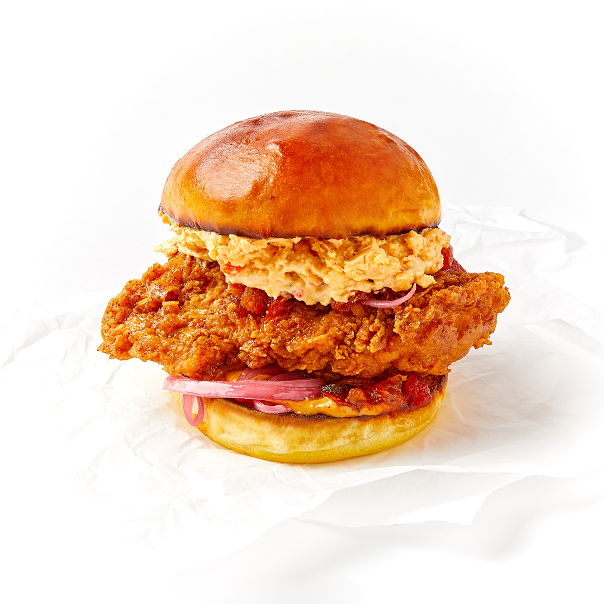 e-commerce food photograph of fried chicken sandwich on parchment paper on white background