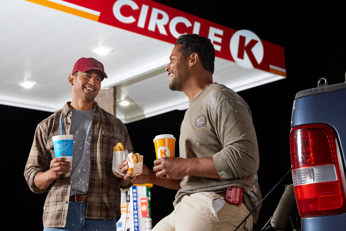 Commercial lifestyle photography of two men eating breakfast sandwiches and drinking polar pop at circle k while refueling their work truck