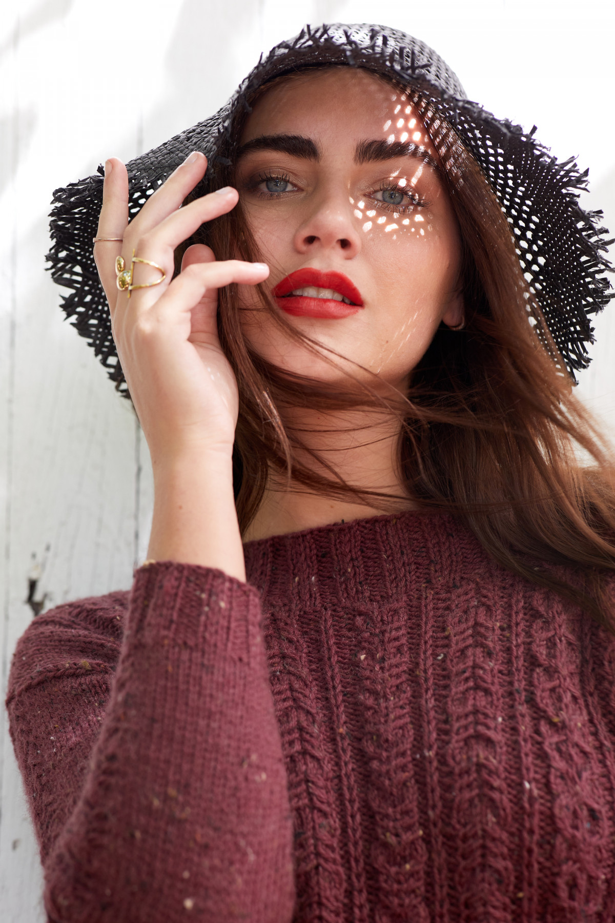 Editorial fashion photo of a female model with long dark hair wearing a straw hat and maroon knit sweater