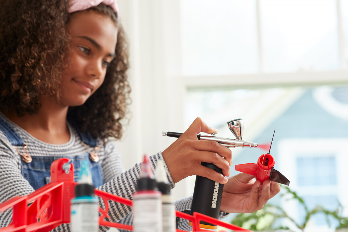 Commercial lifestyle product photography of a young girl using a WORX air brush to paint a model rocket