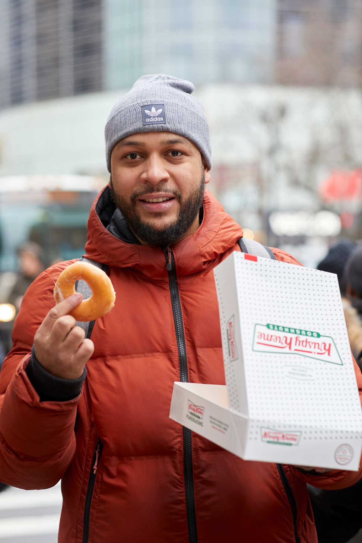 Commercial lifestyle photo of a man in a coat and hat carrying a box of Krispy Kreme doughnuts on the street in NYC