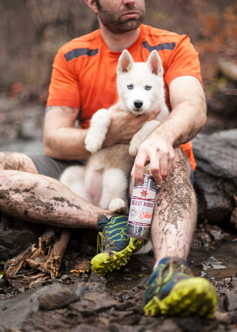 Editorial lifestyle photo of a man outdoors with muddy clothing and a dog holding a canned beverage