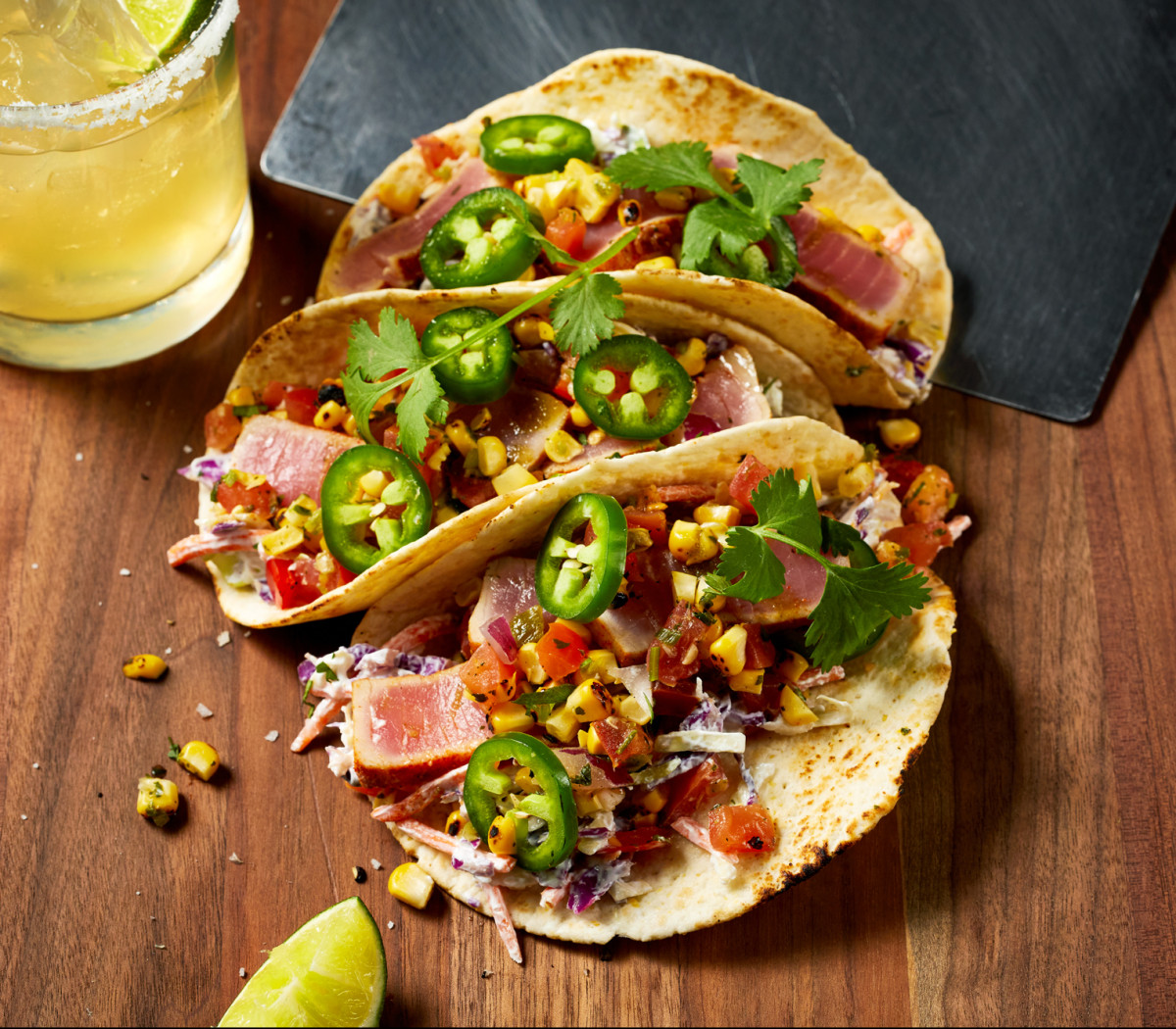 Commercial food photograph of tuna tacos shot top down with margarita and lime on wood table